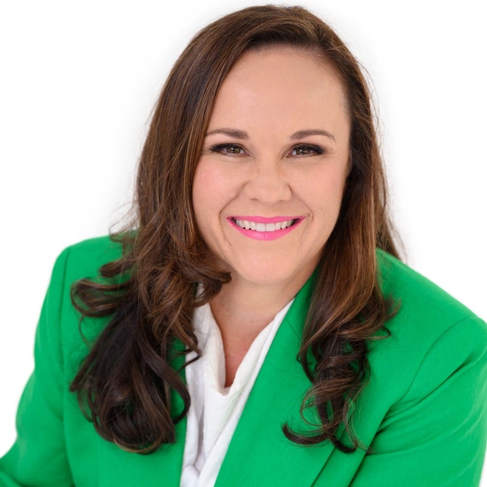 A cropped headshot of Natasha Doherty wearing a green suit, with only the top half of her head and shoulders visible against a plain white backdrop.