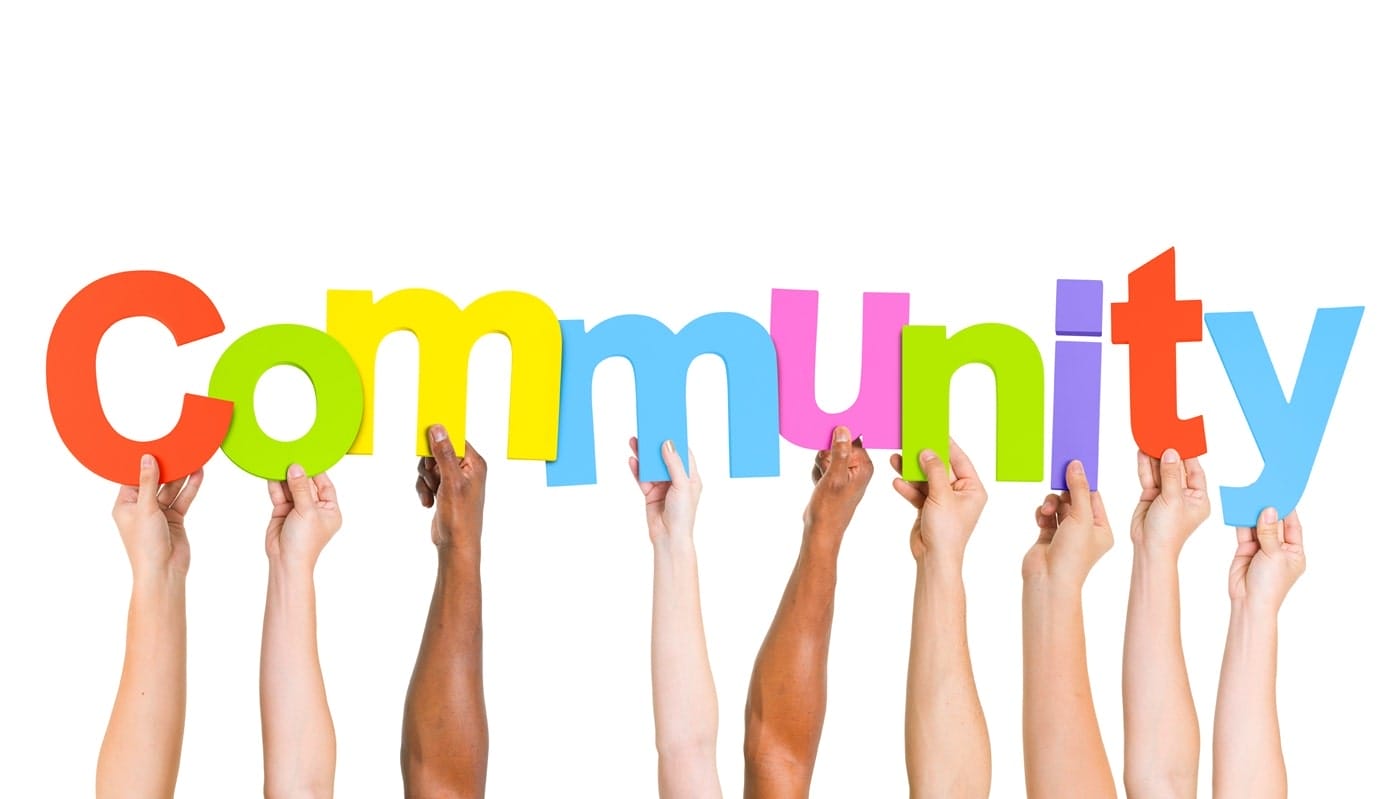 Hands of people from various racial backgrounds holding a sign that says "community," representing unity and shared purpose.