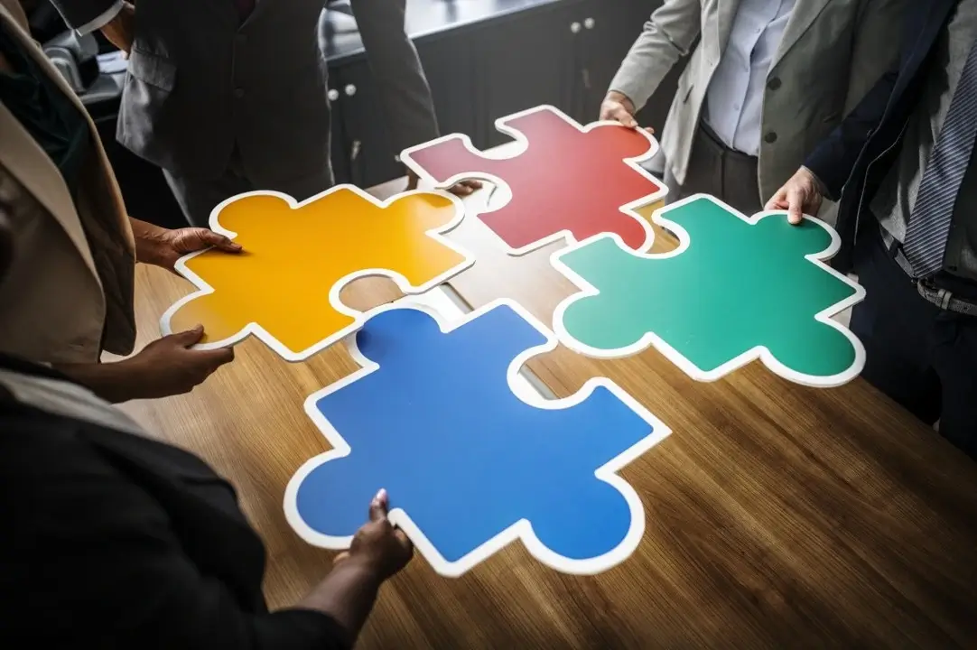 Multiple hands working together to connect colorful puzzle pieces, symbolizing collaboration and teamwork.
